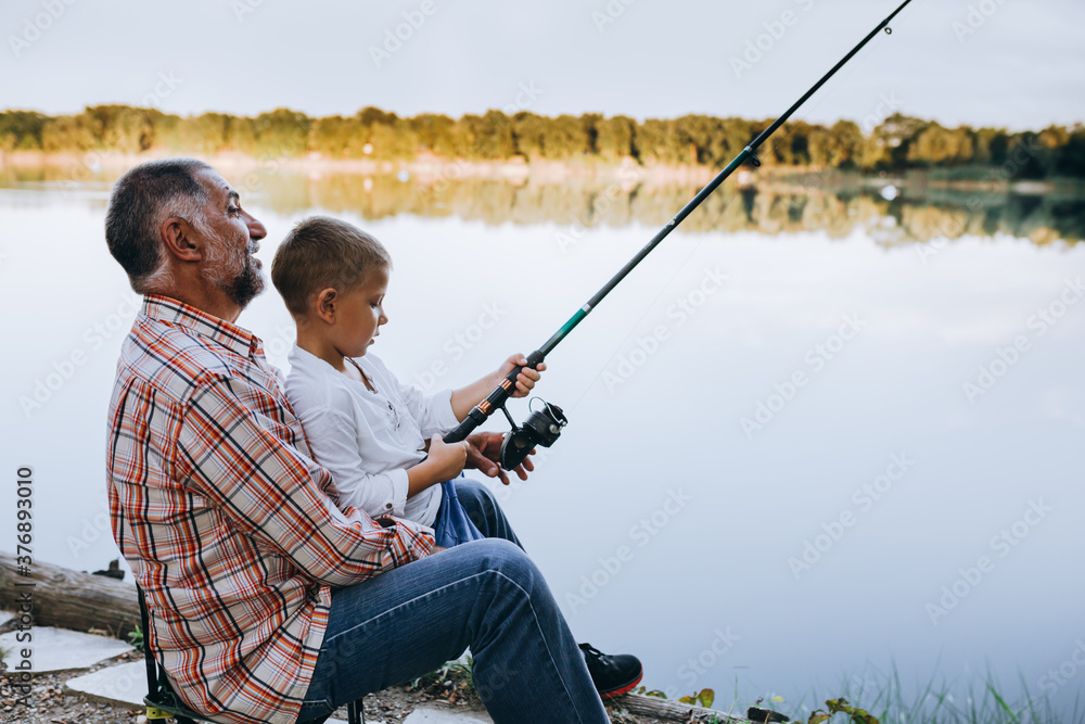 © cherryandbees - grandfather and grandson fishing outdoor on the lake, little boy looking at the camera
