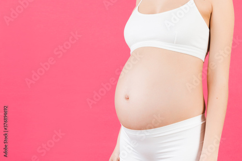 Cropped image of pregnant woman's abdomen at pink background. Future mother is wearing white underwear. Parenting concept. Copy space