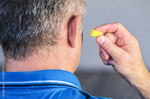 Close - up of a man's ear with a yellow earplug in his hand.