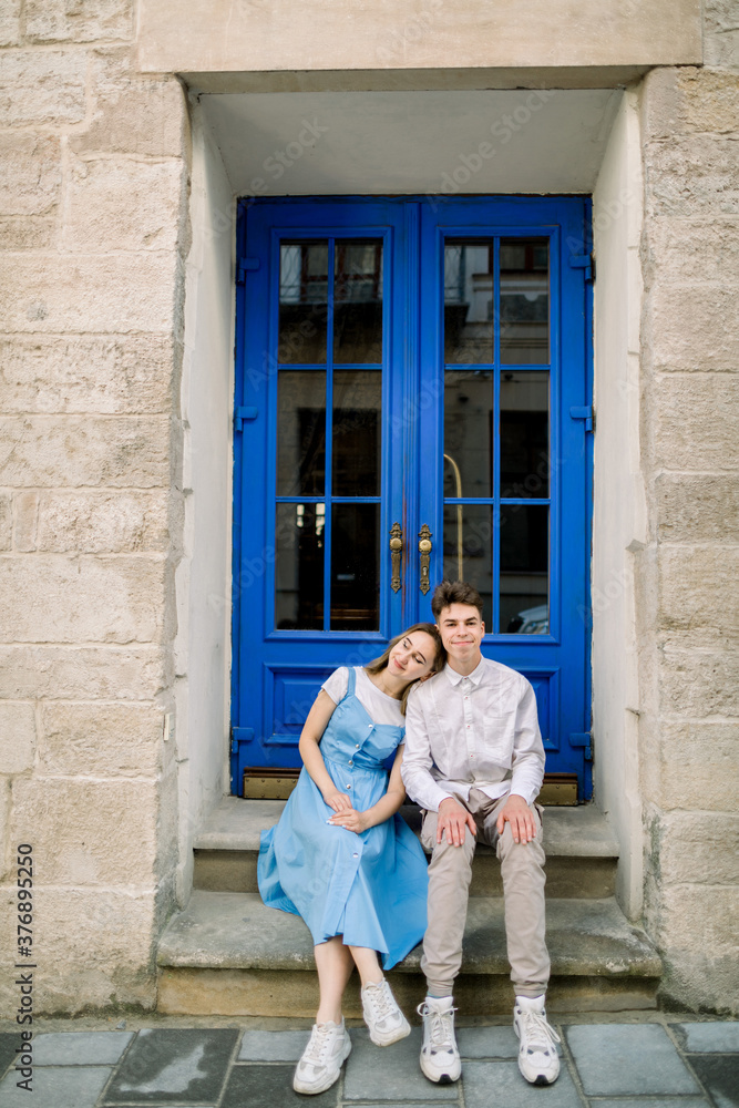 Lovely date on the street. Happy hipster young couple, handsome man with his attractive girlfriend in blue dress, hugging outdoors in the city, posing near beautiful vintage blue door