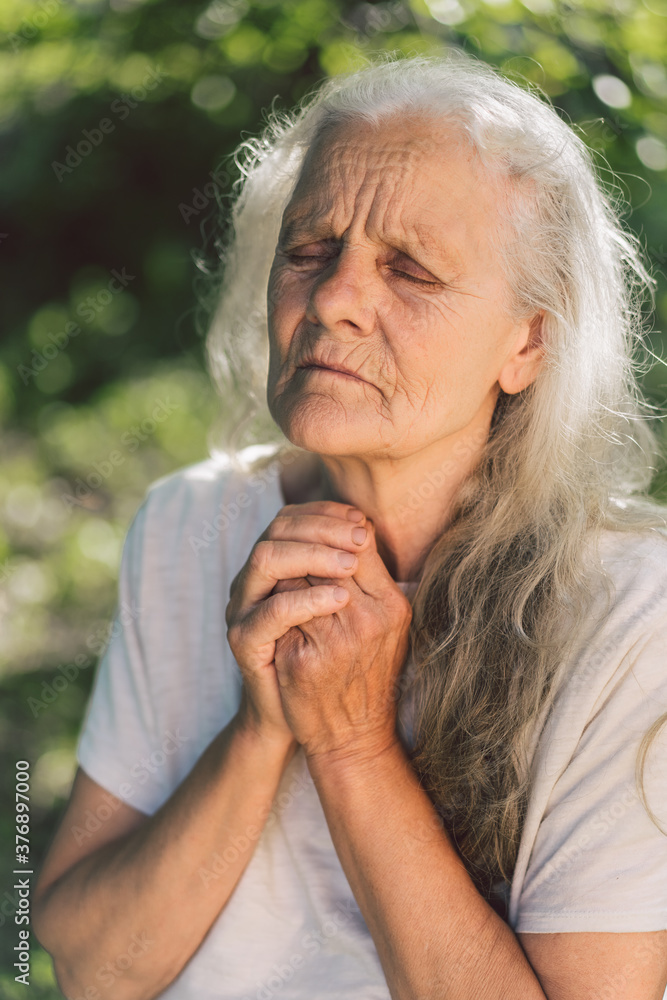 The gray-haired grandmother is praying in outdoors. Faith, spirituality and religion concept. The gray-haired grandmother is praying in outdoors. Faith, spirituality and religion concept.