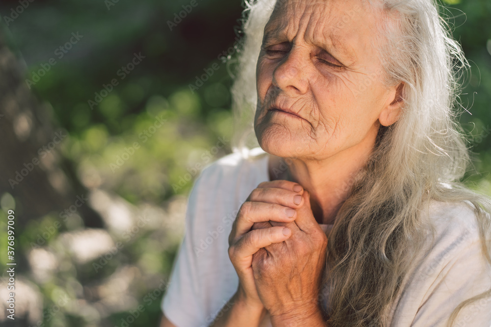 The gray-haired grandmother is praying in outdoors. Faith, spirituality and religion concept. The gray-haired grandmother is praying in outdoors. Faith, spirituality and religion concept.