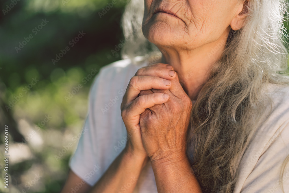 The gray-haired grandmother is praying in outdoors. Faith, spirituality and religion concept. The gray-haired grandmother is praying in outdoors. Faith, spirituality and religion concept.