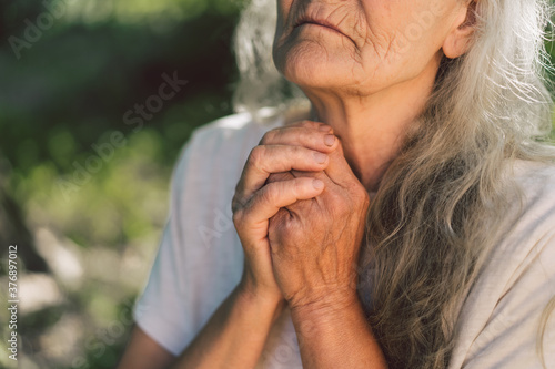 The gray-haired grandmother is praying in outdoors. Faith, spirituality and religion concept. 