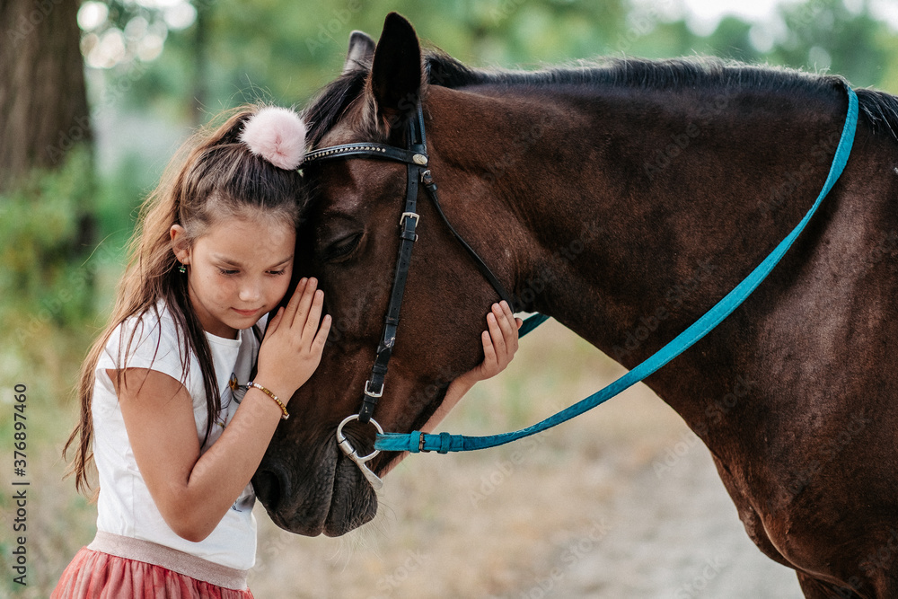 Obraz premium Friendship of a child with a horse. A little girl is affectionately stroking her horse. Walking girls with a horse in the park in autumn.