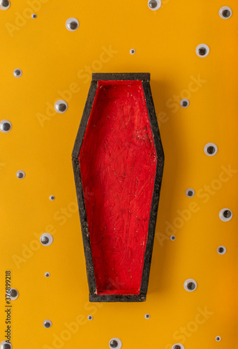 Halloween yellow background with an open red-black coffin in the center, around a scattering of plastic eyes of different sizes. A place for your product.