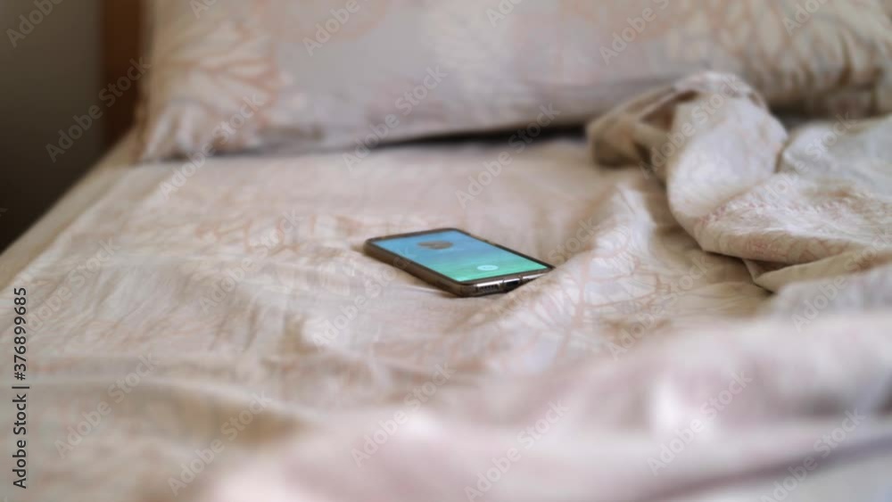 Smartphone that Starts Ringing above an Unmade Bed and a Hand Grabbing it Smartphone that Starts Ringing above an Unmade Bed and a Hand Grabbing it