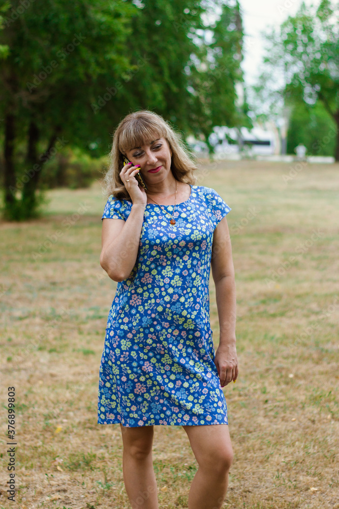 Young blonde woman in a blue dress talking on the phone in the park. Young blonde woman in a blue dress talking on the phone in the park.