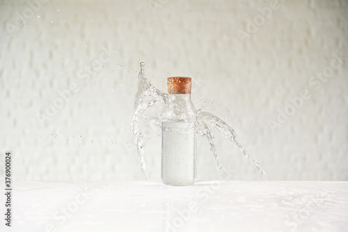 Water splash in the glass cup on the white table, brick wall background.
