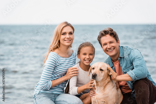 Family with golden retriever looking at camera on beach