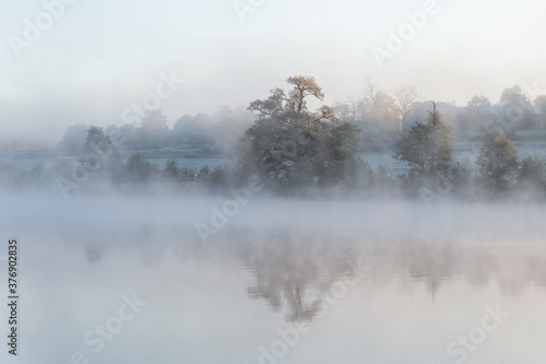 Misty morning, sunrise, fog swirls around autumn landscape. The mist, sunshine and trees create a dreamy scene. Background with place for text, copy space.