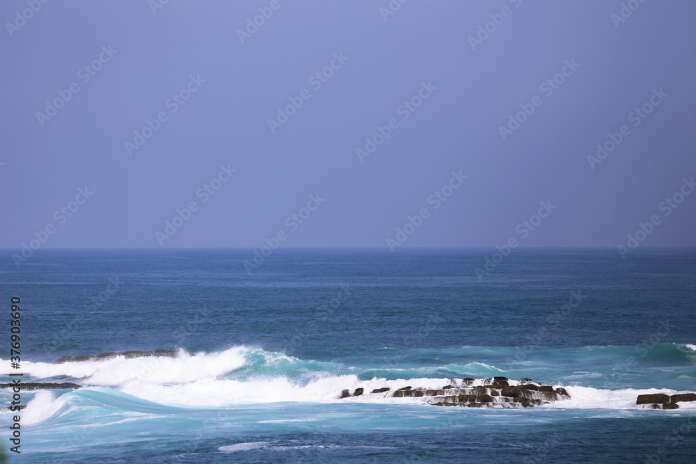 日南海岸の沖の岩場にかかる波