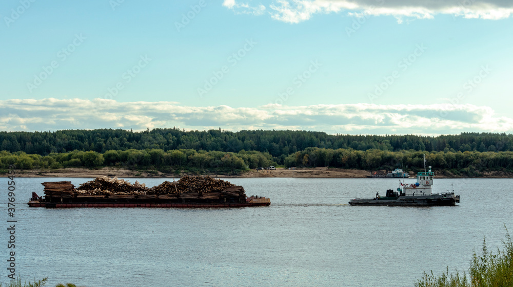 a large boat drags a barge with logs along the river