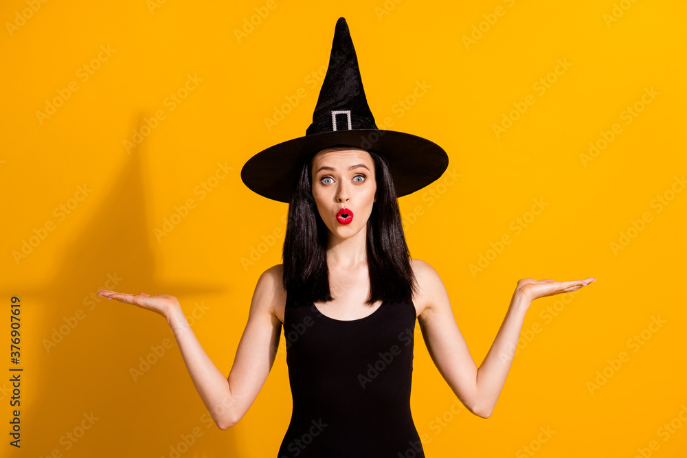Photo of lovely charming young magician lady excited open palms hold empty space allow you choose between best wear black wizard headwear dress isolated bright yellow color background