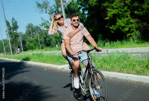 Cheerful young couple having fun riding on bicycle on summer day.