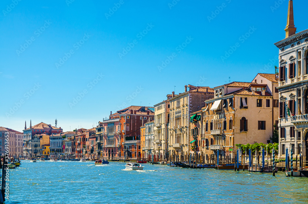 Venice cityscape with Grand Canal waterway, Venetian architecture colorful buildings, wooden pier, yacht boats sailing Canal Grande, blue sky in sunny summer day. Veneto Region, Northern Italy.
