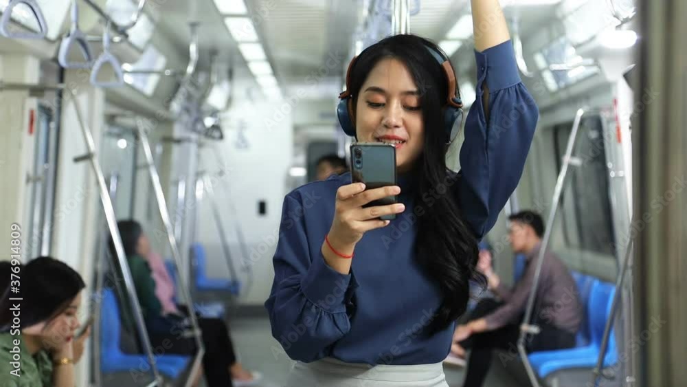 A lifestyle of young Asian woman using cellphone with headset while taking the subway train to work at the rush hour morning A lifestyle of young Asian woman using cellphone with headset while taking the subway train to work at the rush hour morning