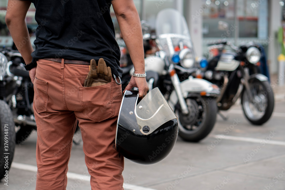 Young Biker standing and holding helmet and gloves beside motorcycle.Trip and lifestyle of motorbike concept Young Biker standing and holding helmet and gloves beside motorcycle.Trip and lifestyle of motorbike concept
