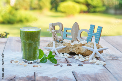 Green smoothie with natural seeds and mint, on wooden table with sand, shells, rocks and starfish. photo