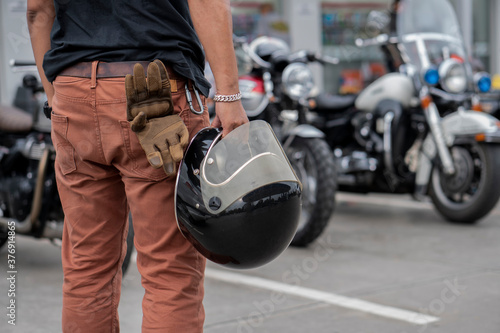 Young Biker standing and holding helmet and gloves beside motorcycle.Trip and lifestyle of motorbike concept