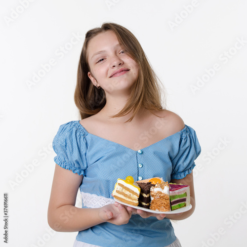 Teenager girl in blue dress holds plate of cream sweet cakes and smiles, Studio portrait on white background
