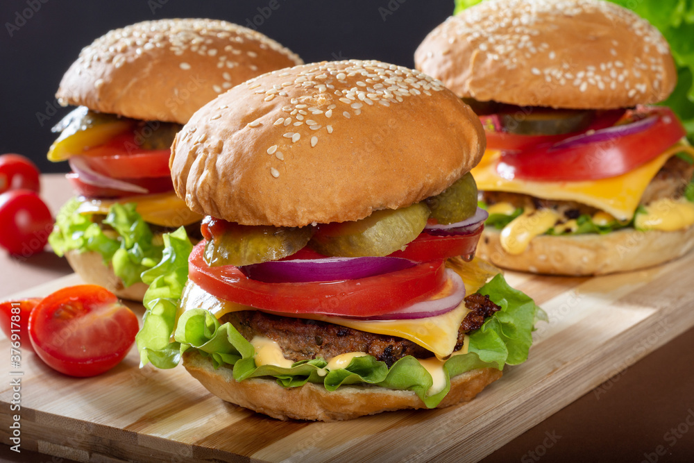 Large Burger with beef Patty on a wooden Board. Burger with tomatoes and pickles. Classic Burger. Large Burger with beef Patty on a wooden Board. Burger with tomatoes and pickles. Classic Burger.
