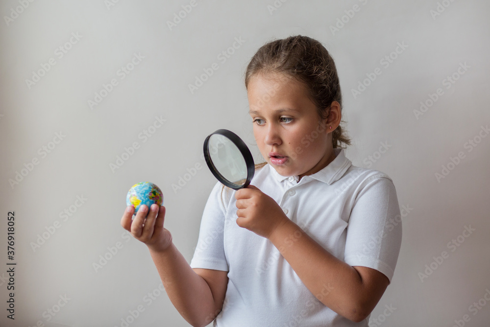 Little girl with magnifier looking at little globe on gray background Little girl with magnifier looking at little globe on gray background