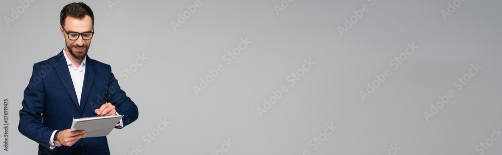 horizontal image of businessman in blue blazer and eyeglasses signing document isolated on grey horizontal image of businessman in blue blazer and eyeglasses signing document isolated on grey