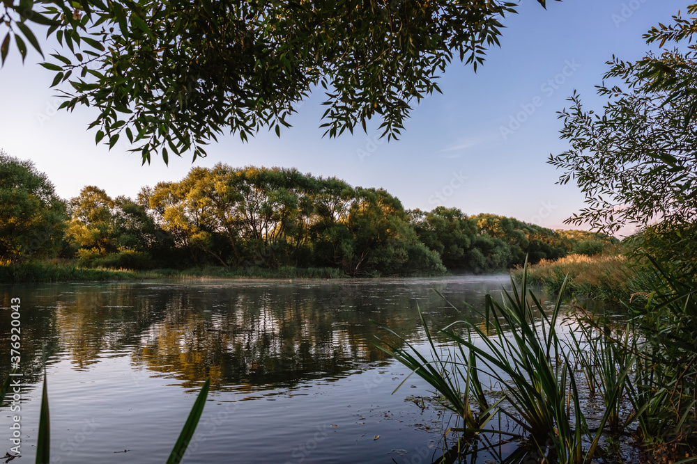 Obraz premium Summer or autumn sunrise over the river. Calm water flow, morning fog and birds. Natural beauty of pristine nature. Water protection zone. Beautiful landscape banner, postcard or desktop wallpaper