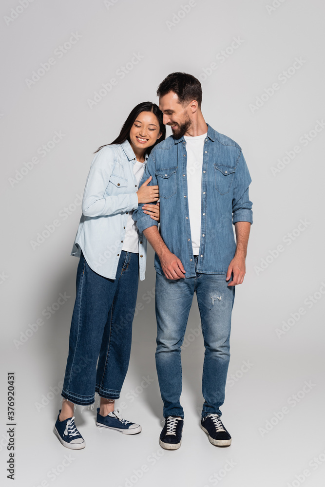 full length view of young asian woman with closed eyes leaning on stylish boyfriend on grey full length view of young asian woman with closed eyes leaning on stylish boyfriend on grey