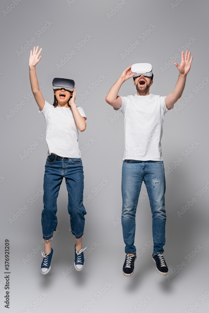 excited couple in vr headsets, jeans and white t-shirts waving hands while  levitating in vr headsets on grey foto de Stock | Adobe Stock