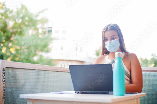 Head shot young woman working from home wearing protective mask