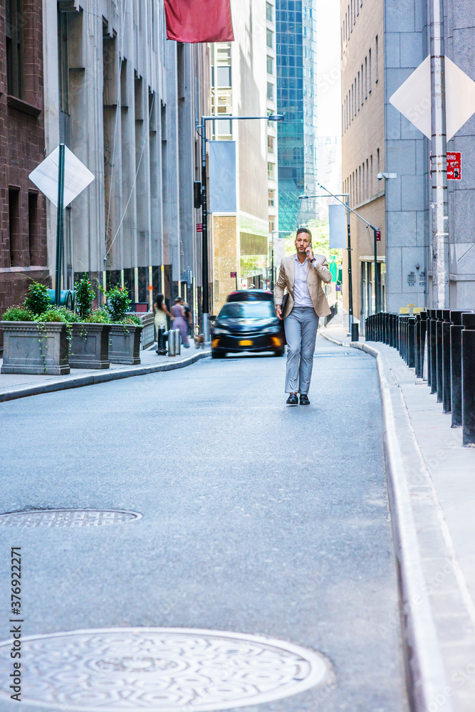 European Businessman traveling, working in New York City, with beard, little gray hair, wearing beige blazer, gray pants, leather shoes, holding briefcase, walking on street, talking on cell phone..