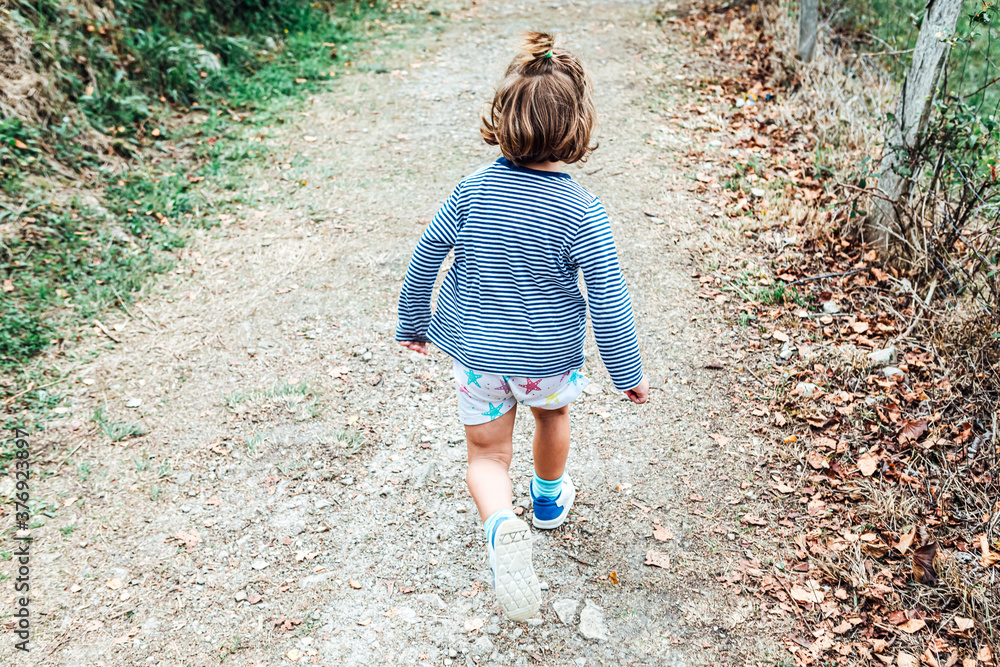 Little blond hair girl walking along a path in a forest. Nature concept Little blond hair girl walking along a path in a forest. Nature concept