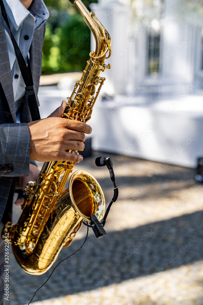 Obraz premium Young man playing the saxophone at the wedding. Blurred background. Selective focus.