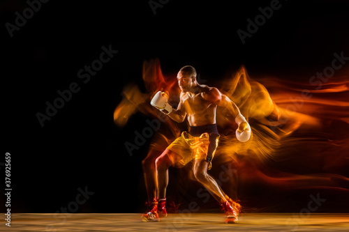 In fire. Professional boxer training isolated on black studio background in mixed light. Man in gloves practicing in kicking and punching. Healthy lifestyle, sport, workout, motion and action concept.