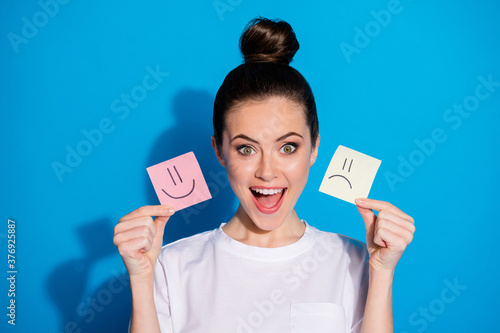 Close-up portrait of her she nice-looking attractive lovely pretty cheerful cheery glad girl holding in hand stwo different emotion papers isolated on bright vivid shine vibrant blue color background photo