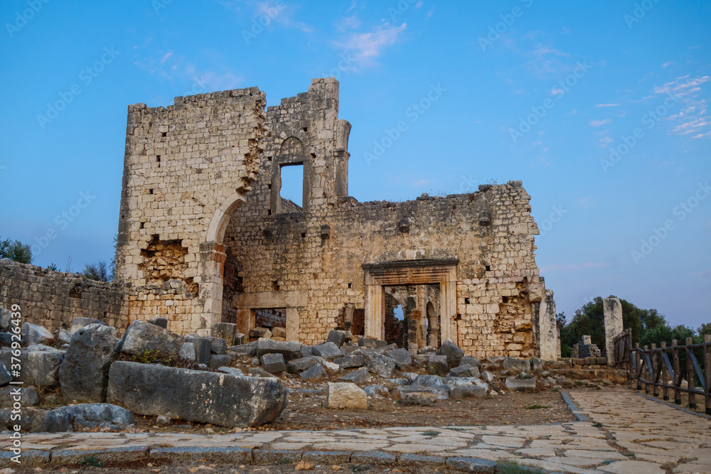 Evening view onto remains of gates & walls of basilica in ancient city Kanli Divane or Canytelis, Ayaş, Turkey. It's built in 2 century AD. Building stands near sinkhole (it's fenced, right side)
