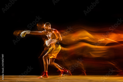 Fireball. Professional boxer training isolated on black studio background in mixed light. Man in gloves practicing in kicking and punching. Healthy lifestyle, sport, workout, motion and action concept