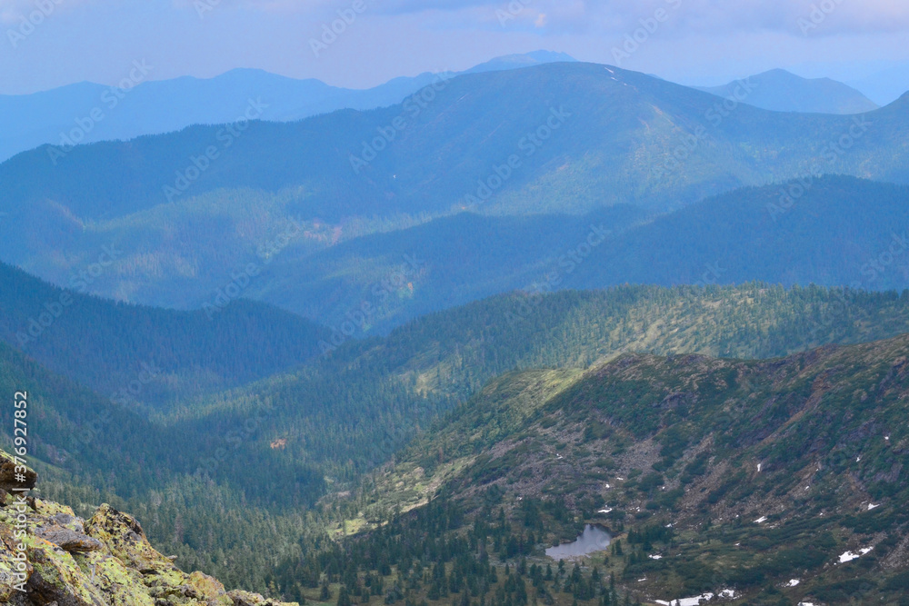 view of mountain small lake among snowy glaciers, green emerald blue mountain ridges overgrown with trees, Chersky peak