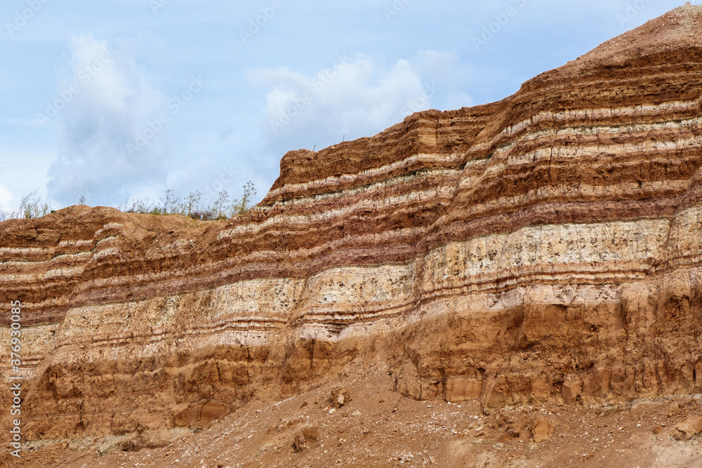 Earth wall in industrial quarry with open-pit mining. It can be seen very clearly underground layers of useful minerals