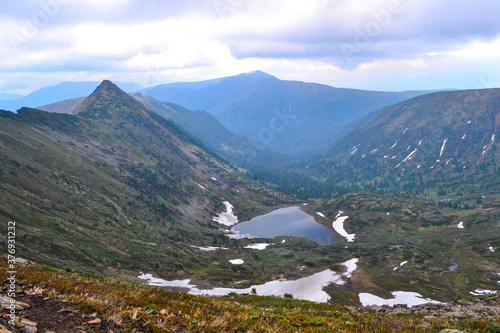 small mountain lake in the form of a heart among snowy glaciers, green mountain ranges overgrown with trees, Chersky peak photo