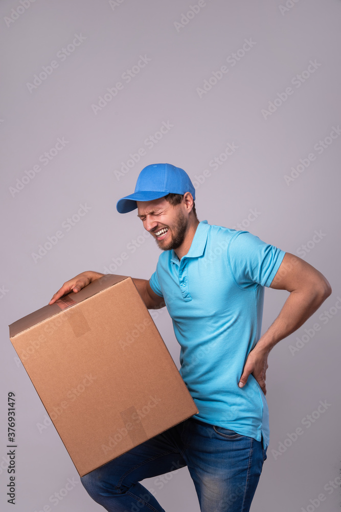 Delivery man suffering from a back pain while carrying heavy box Delivery man suffering from a back pain while carrying heavy box