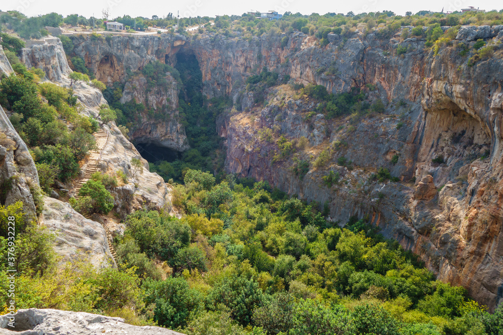 Panoramic view onto bluff walls & bottom of karst sinkhole called Cennet (Heaven), Kizkalesi, Turkey. It's one of largest sinkholes in Turkey. Its depth about 70 m, square about 250x110 m
