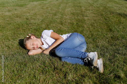 Light-haired european child lies on green grass. Rest in the park. 