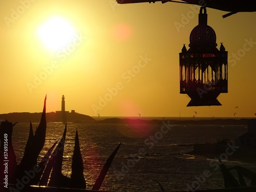 sunset at the trafalgar lighthouse, barbate, cadiz, andalucia, southern Spain with backlit kitesufers in atlantic ocean with arabic lantern hanging in the foreground