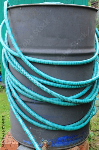 The green hose is wound around an old barrel. Russia.