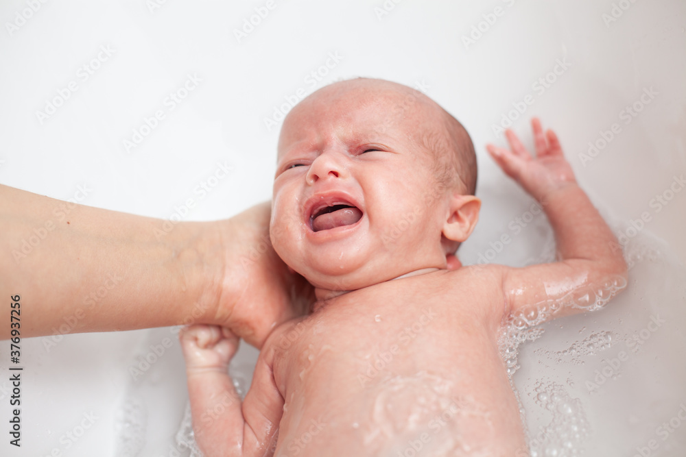 Newborn baby is being bathed by his mother. Newborn baby crying in bath time