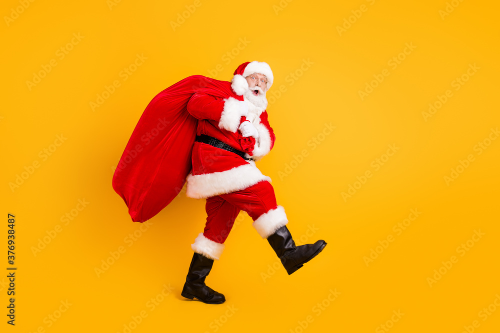 Full length body size profile side view of his he nice funny cheery amazed white-haired Santa carrying big large sack custom tradition isolated bright vivid shine vibrant yellow color background Full length body size profile side view of his he nice funny cheery amazed white-haired Santa carrying big large sack custom tradition isolated bright vivid shine vibrant yellow color background