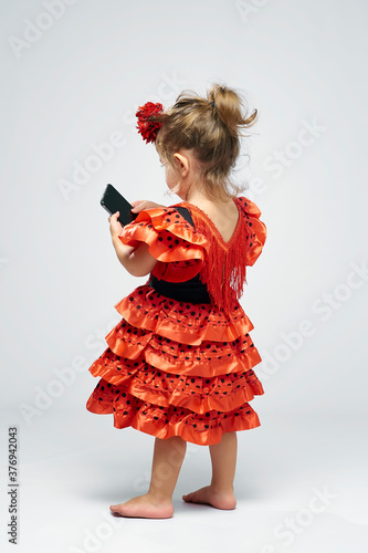 2 year old girl dressed in a typical Spanish flamenco dress in a studio  with white background using a mobile Stock-foto | Adobe Stock